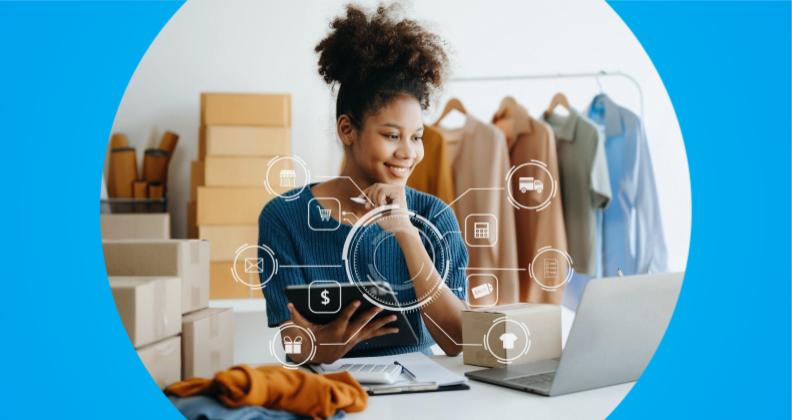Empreendedora usando um laptop cercado por ícones digitais relacionados a negócios on-line e remessas, com caixas de papelão e cabides de roupas ao fundo.