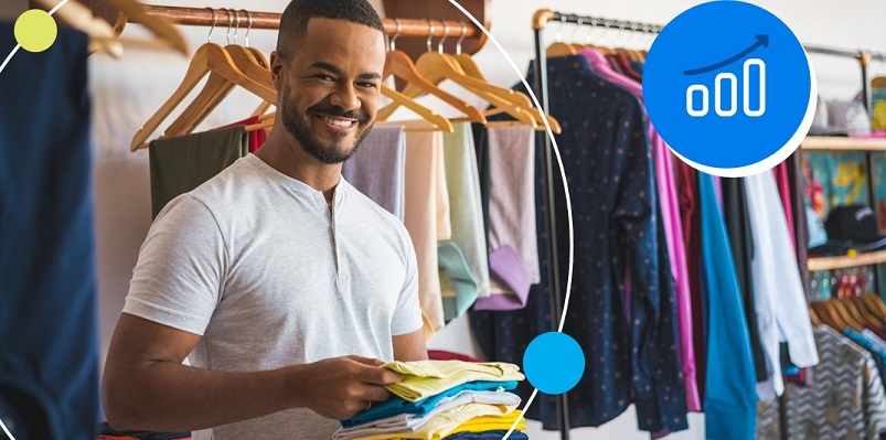 Empreendedor de loja de roupas com largo sorriso ao pensar em superar sua meta de vendas.