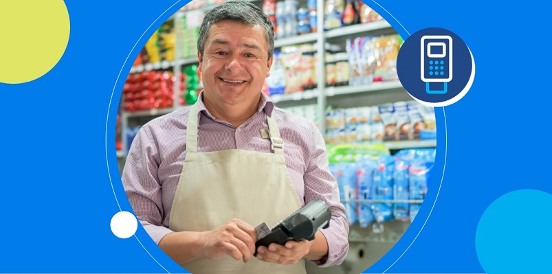 Dono de mercadinho com maquininha na mão sorri após entender melhor se tem ou não que declarar renda.